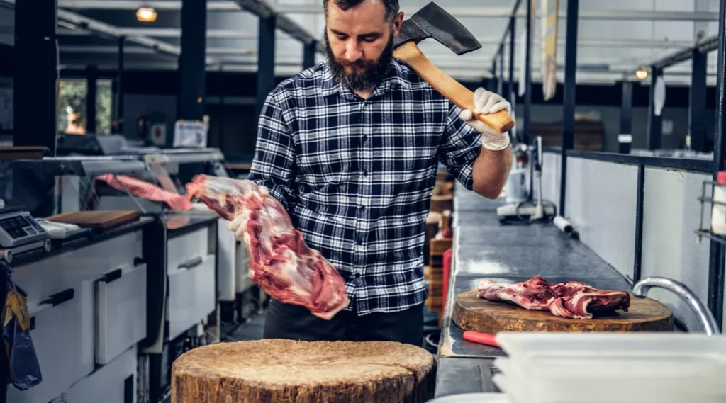 Un homme tient un couteau à viande en train de couper de la viande sur une planche à découper.