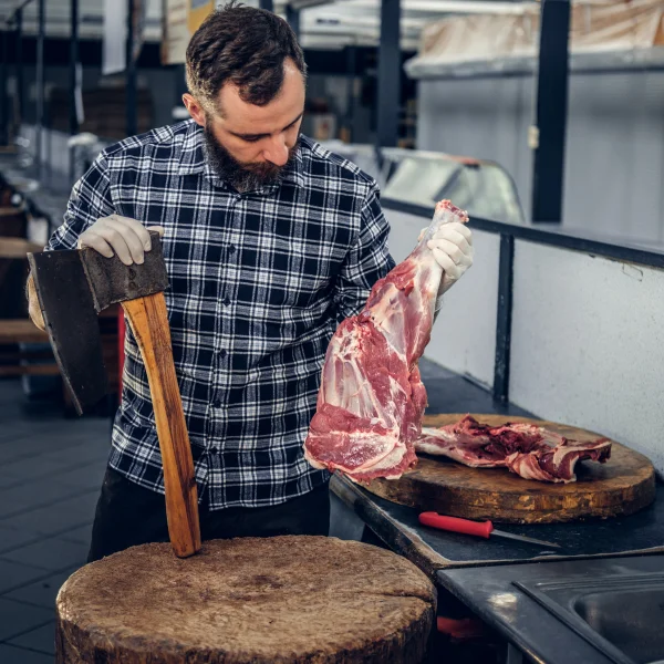 Un homme découpe de la viande sur une table en bois.