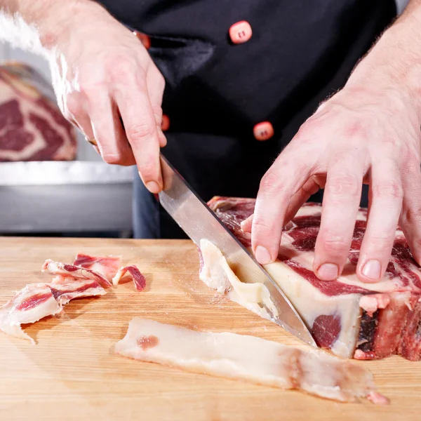 Un homme découpe de la viande sur une planche à découper en bois.
