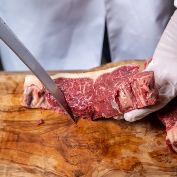 Une personne découpe un morceau de viande avec un couteau sur une planche à découper.